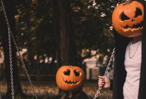 An adult and a child wearing carved jack-o'-lantern masks on a park swing, for a guide to the best Halloween neighborhoods in Marin